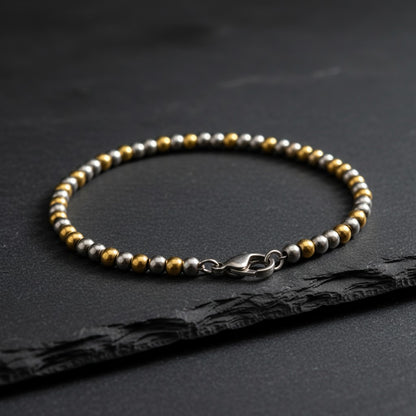 Aramat Jewels bicolor stalen kralenarmband met zilver- en goudkleurige bolletjes, 19 cm lang en 4 mm breed.