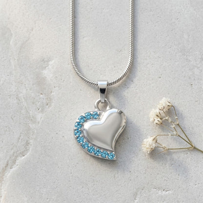 Aramat Jewels zilverkleurige stalen ashanger in hartvorm met blauwe zirkonia steentjes. Een elegant gedenksieraad.